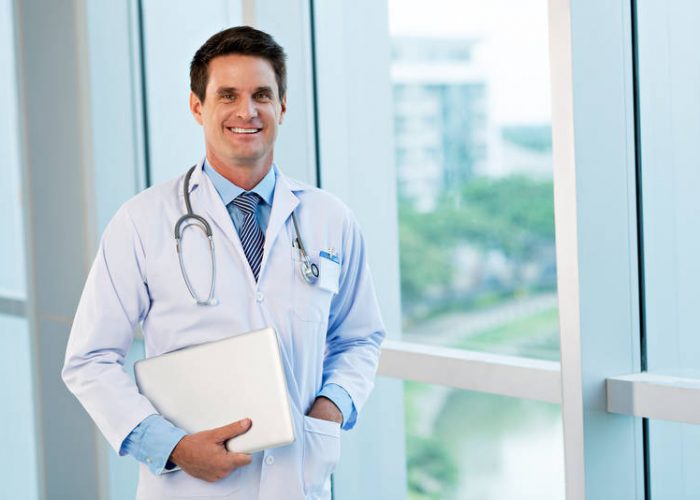 Happy doctor standing with a laptop