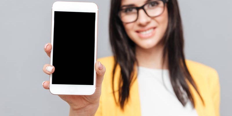 Woman showing phone display to camera over grey background